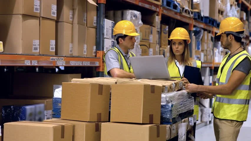Warehouse Warehouse team discussing inventory among stacked boxes: Illustrating The Transformative Impact of Warehouse Design Consultants on Your Business.
