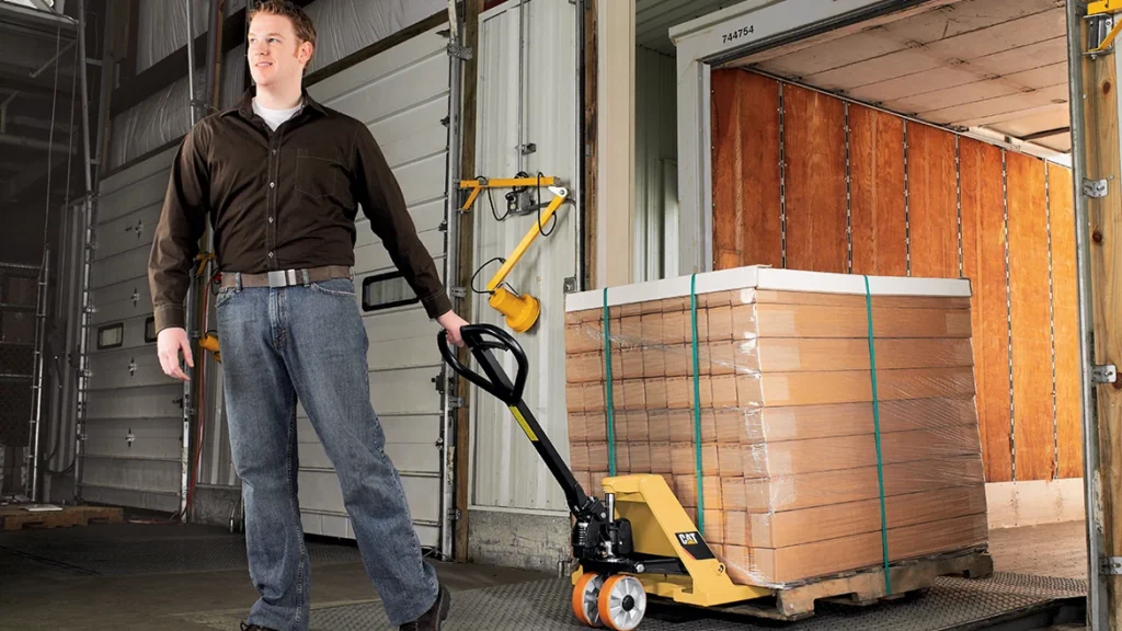Man pulling yellow hydraulic pallet jack with wrapped boxes towards a truck. Advantages of hydraulic pallet jacks.