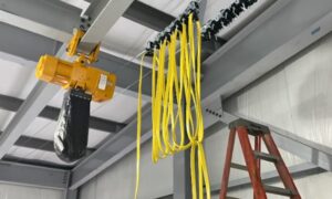 A yellow hoist with black chain and cables, showing how hoists reduce worker strain in warehouses.