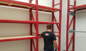 A person assembling red heavy-duty industrial shelving, illustrating support for FIFO and LIFO inventory systems.