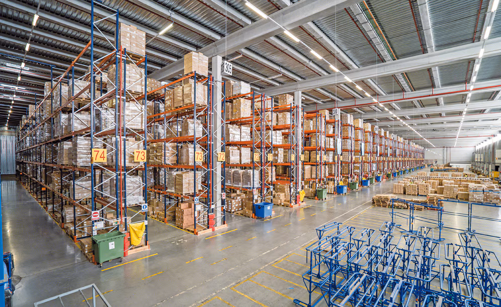 Warehouse A well-lit industrial workshop with a large yellow 'KUNDEL 2 TON' overhead crane, scattered tools and machinery, a mezzanine staircase, and a bay door revealing a truck outside.