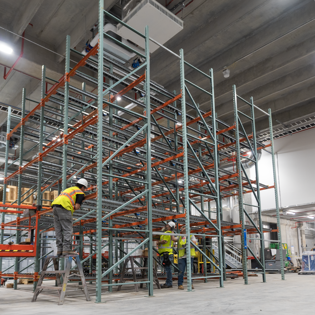 Website-Photo_installation_2 MWS installer on a scissor lift assembling blue and yellow pallet rack uprights and beams in a warehouse